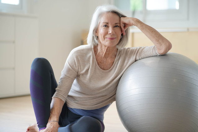 grey-haired woman sitting with exercise ball 